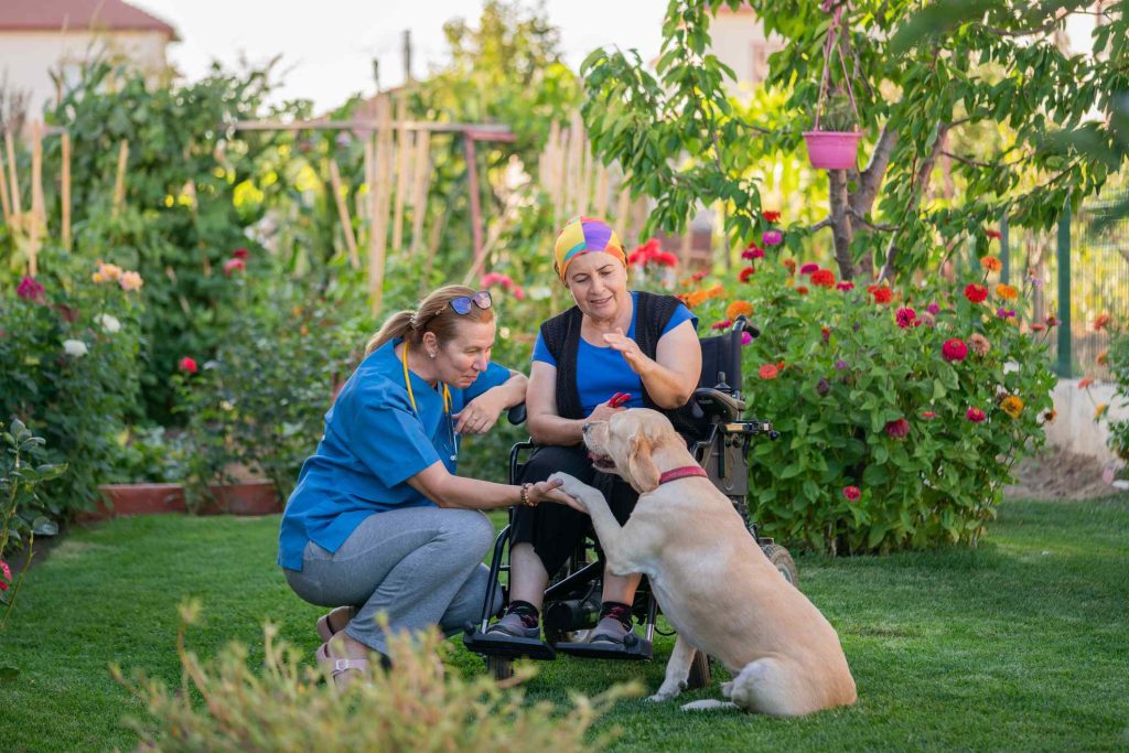 A woman kneels next to a woman in a wheelchair with a guide dog.